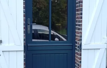 Porte d’entrée PVC bleu foncé avec vitrage, installée entre volets battants blancs
