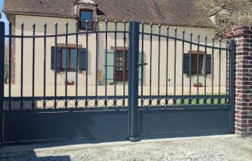 Portail aluminium gris à deux vantaux avec barreaux décoratifs, installé devant une maison individuelle