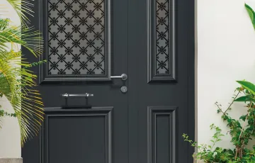 Porte d’entrée noire avec vitrage décoratif et poignée moderne, intégrée à une entrée extérieure